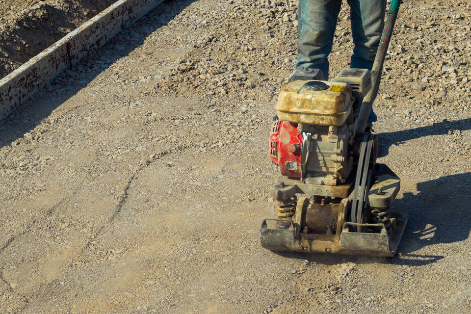 Person compacting the gravel patio base using a plate compactor