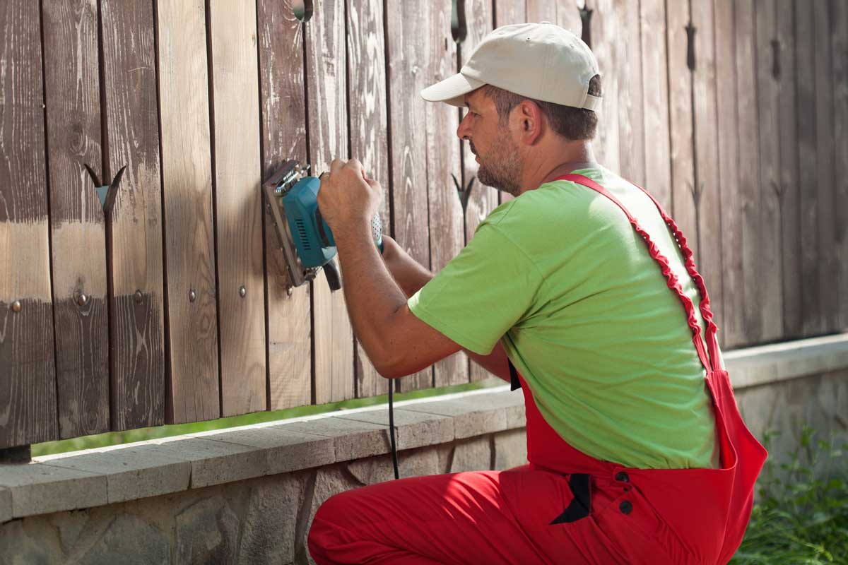 Painter prepping a fence for stain by sanding the surface