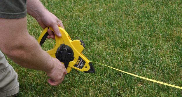 Fence installer using a tape measure to lay out a fence