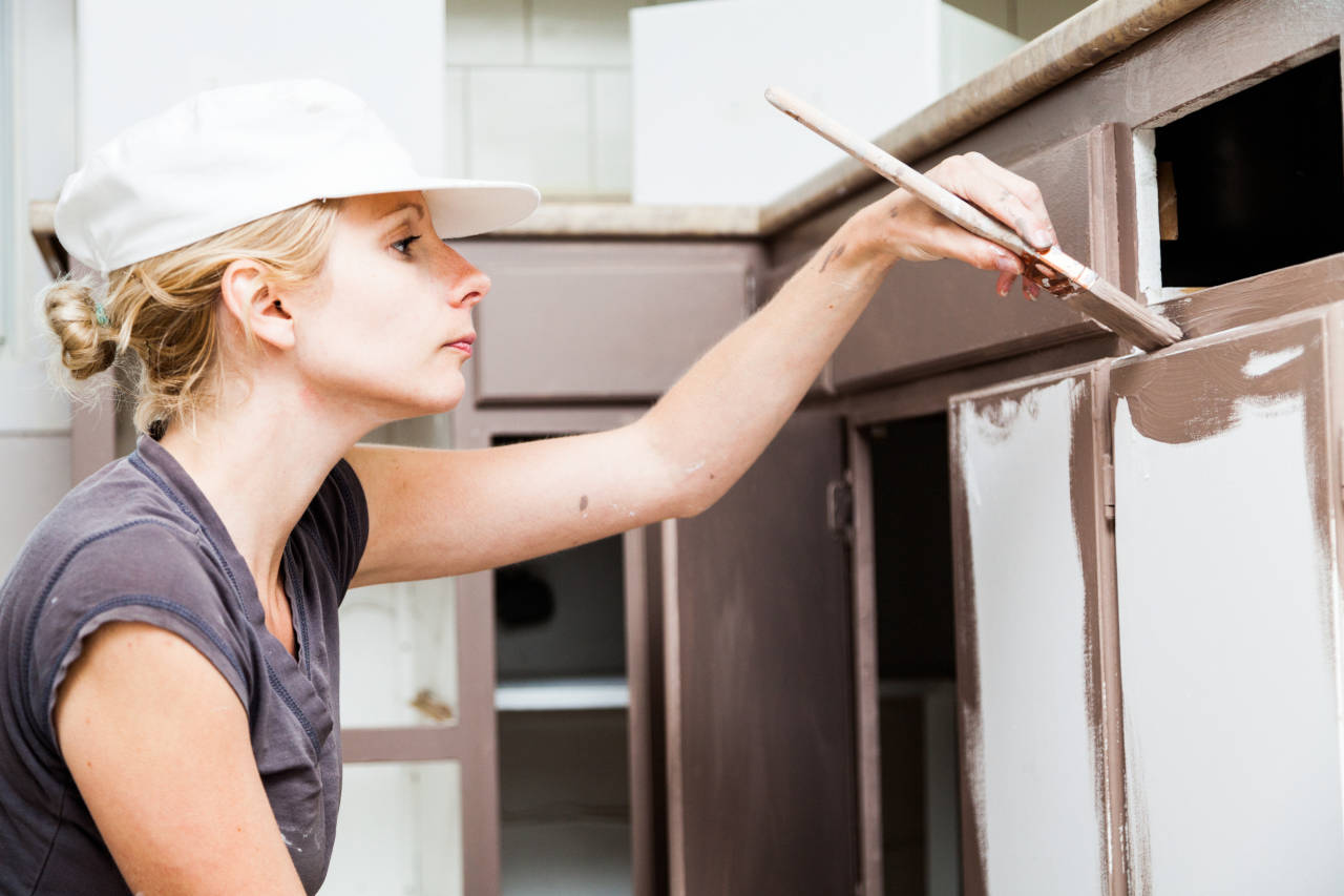 Person painting kitchen cabinets using a brush