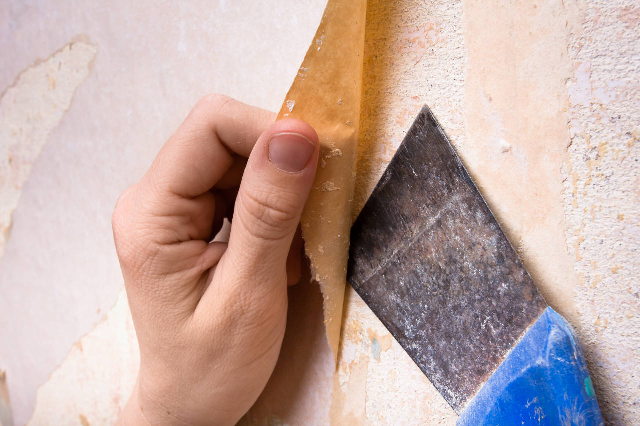 Person removing wallpaper using a scraper