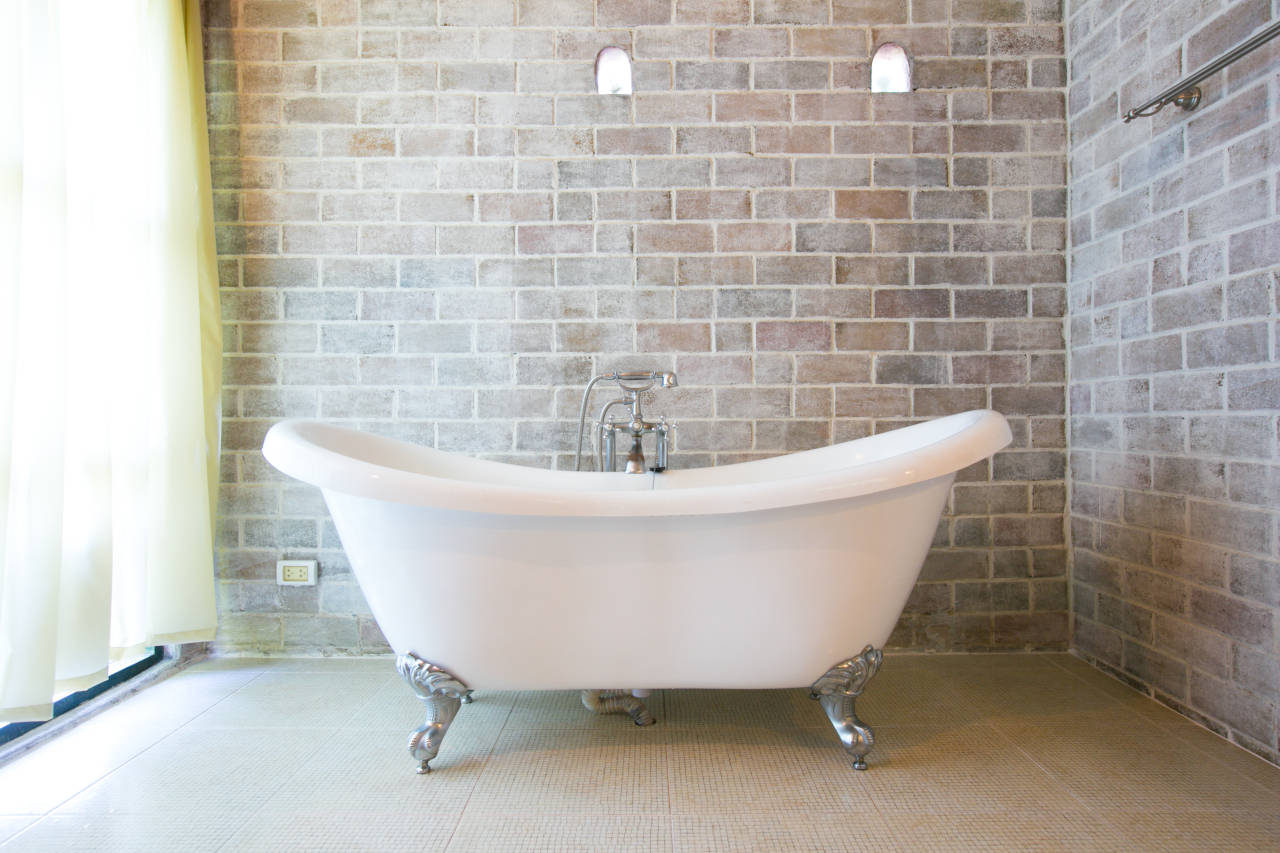 cast iron clawfoot bathtub in a bathroom with brick walls