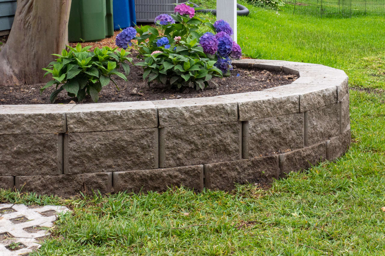 Retaining wall composed of standard block and cap block in a landscaping bed